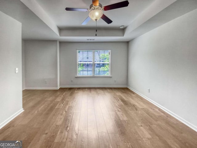 spare room with a tray ceiling, ceiling fan, and light wood-type flooring