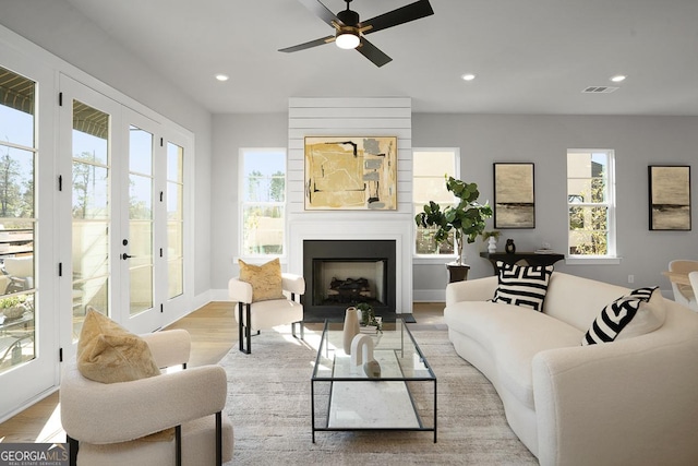 living room featuring ceiling fan, a fireplace, light hardwood / wood-style flooring, and a wealth of natural light