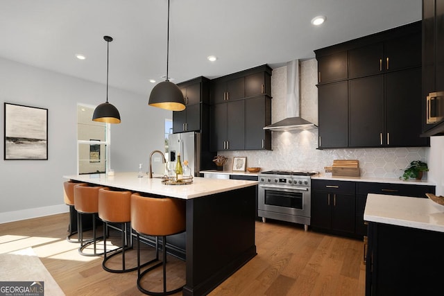 kitchen with decorative light fixtures, an island with sink, a kitchen breakfast bar, premium appliances, and wall chimney exhaust hood