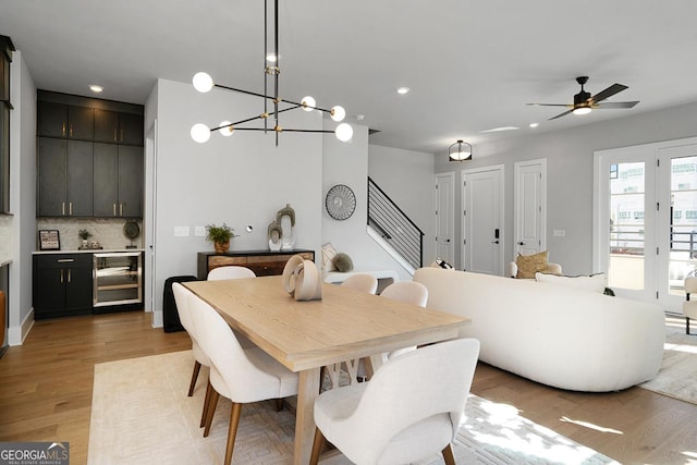 dining room with ceiling fan with notable chandelier, light hardwood / wood-style floors, and beverage cooler