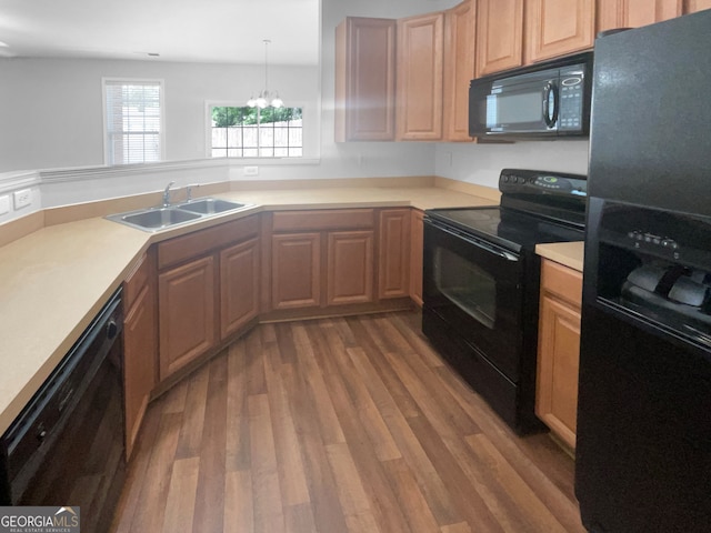 kitchen with hanging light fixtures, black appliances, an inviting chandelier, sink, and hardwood / wood-style flooring