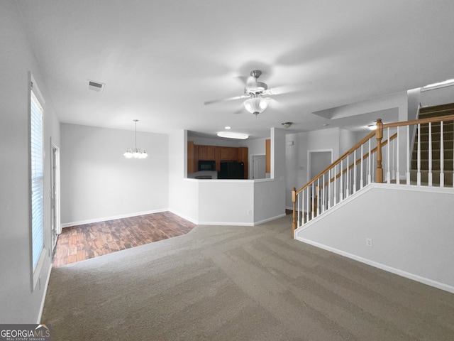 unfurnished living room featuring ceiling fan with notable chandelier and dark colored carpet