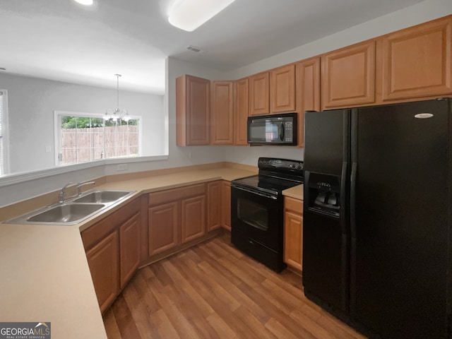 kitchen with decorative light fixtures, light hardwood / wood-style flooring, black appliances, sink, and a notable chandelier