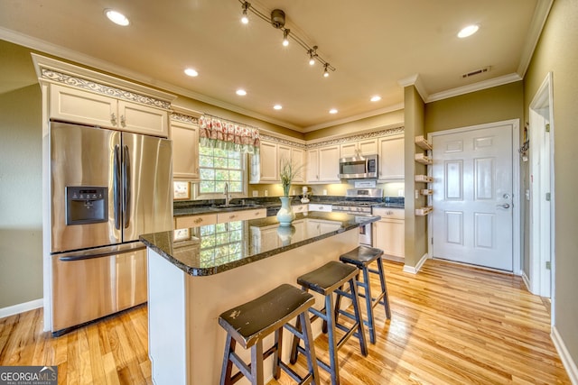 kitchen featuring a center island, light hardwood / wood-style flooring, rail lighting, stainless steel appliances, and a kitchen bar