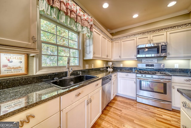 kitchen featuring appliances with stainless steel finishes, light hardwood / wood-style flooring, dark stone counters, sink, and ornamental molding