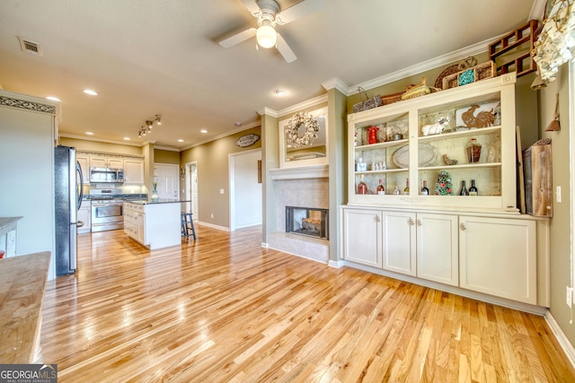 interior space featuring ornamental molding, a tile fireplace, ceiling fan, and light wood-type flooring