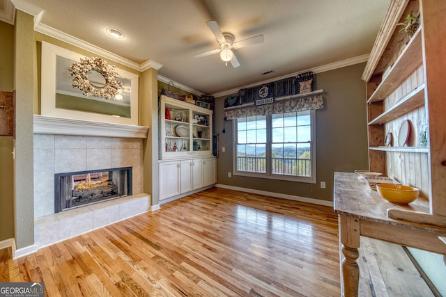 interior space featuring light hardwood / wood-style flooring, crown molding, ceiling fan, and a fireplace