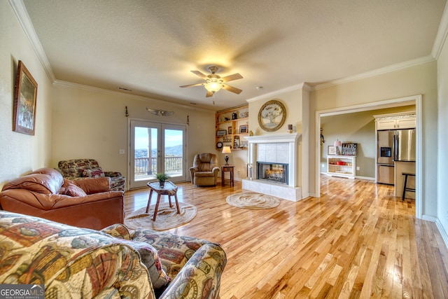 living room featuring ornamental molding, a fireplace, a textured ceiling, and light wood-type flooring