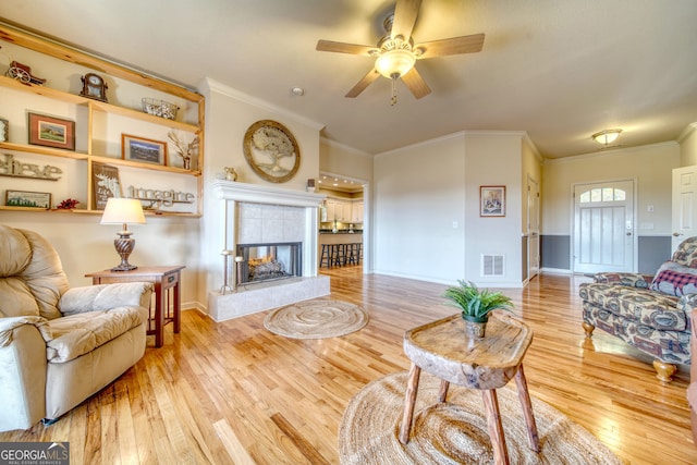 living room featuring wood-type flooring, ceiling fan, crown molding, and a fireplace