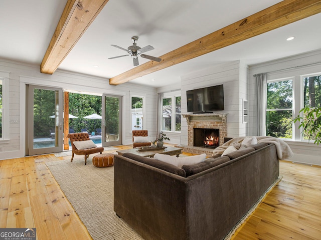 living room with beamed ceiling, plenty of natural light, light hardwood / wood-style floors, and a brick fireplace