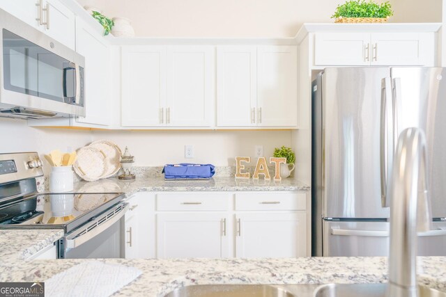 kitchen featuring light stone countertops, stainless steel appliances, and white cabinets