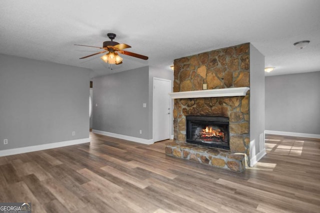 unfurnished living room featuring a stone fireplace, ceiling fan, hardwood / wood-style flooring, and a textured ceiling