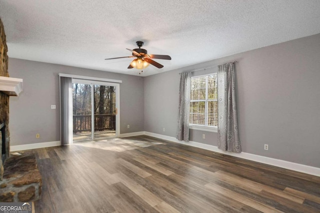 empty room with a textured ceiling, ceiling fan, a fireplace, and dark wood-type flooring