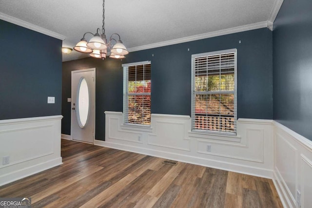 empty room featuring ornamental molding, a notable chandelier, a textured ceiling, and dark wood-type flooring