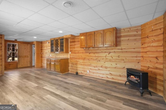 interior space with a paneled ceiling, hardwood / wood-style flooring, a wood stove, and wood walls