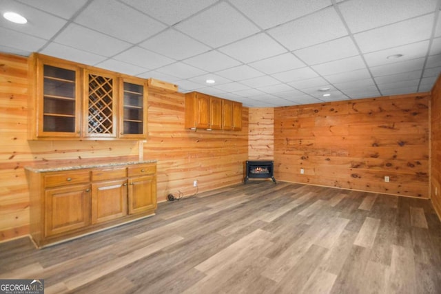 interior space with wood walls, wood-type flooring, light stone counters, a wood stove, and a paneled ceiling