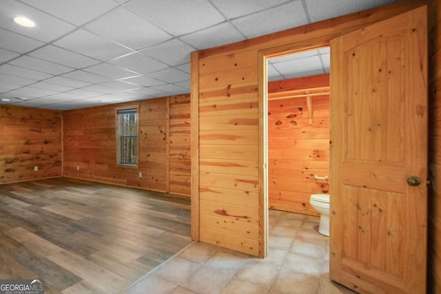 interior space with a drop ceiling, tile floors, and wooden walls