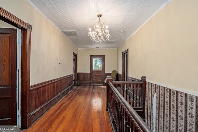 hall with a notable chandelier, dark hardwood / wood-style floors, crown molding, and wooden walls