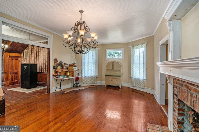 unfurnished dining area featuring crown molding, a fireplace, wood-type flooring, and a notable chandelier