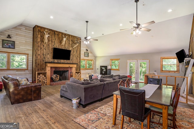 living room featuring a brick fireplace, ceiling fan, hardwood / wood-style flooring, high vaulted ceiling, and wood walls