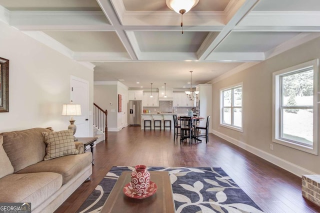 living room with beam ceiling, coffered ceiling, crown molding, dark wood-type flooring, and a notable chandelier