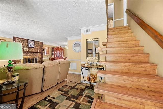 living room with ornamental molding, a stone fireplace, hardwood / wood-style floors, and a textured ceiling