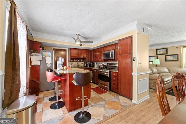 kitchen with ornamental molding, appliances with stainless steel finishes, a kitchen bar, ceiling fan, and a textured ceiling