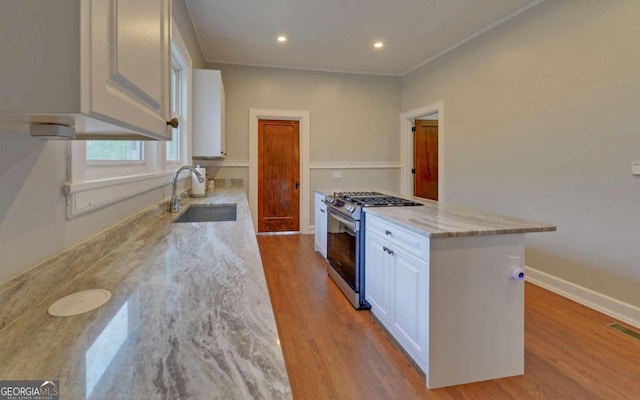 kitchen featuring light stone countertops, sink, light hardwood / wood-style flooring, white cabinetry, and stainless steel gas range