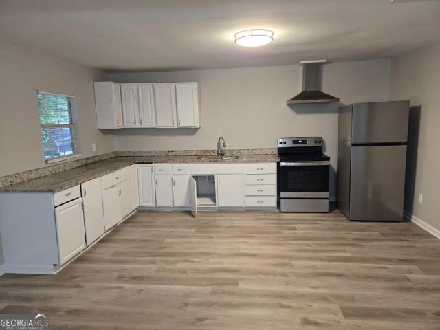 kitchen featuring light hardwood / wood-style flooring, stainless steel appliances, wall chimney exhaust hood, white cabinetry, and sink