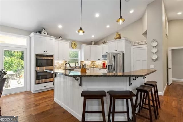 kitchen featuring pendant lighting, white cabinetry, appliances with stainless steel finishes, hardwood / wood-style flooring, and tasteful backsplash