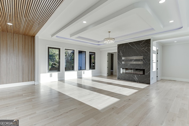 unfurnished living room featuring a raised ceiling, crown molding, a notable chandelier, a premium fireplace, and light hardwood / wood-style floors