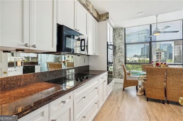 kitchen with ceiling fan, light hardwood / wood-style floors, white cabinetry, black appliances, and dark stone countertops