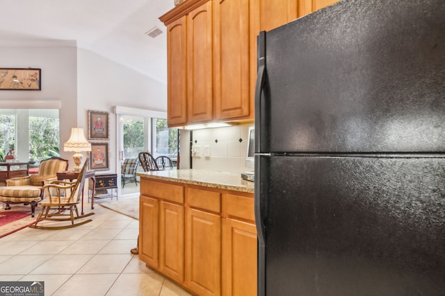 kitchen featuring a wealth of natural light, light tile flooring, vaulted ceiling, and black fridge