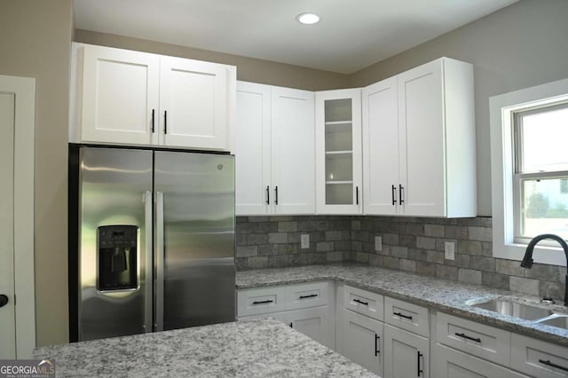 kitchen with backsplash, sink, stainless steel fridge with ice dispenser, and white cabinetry