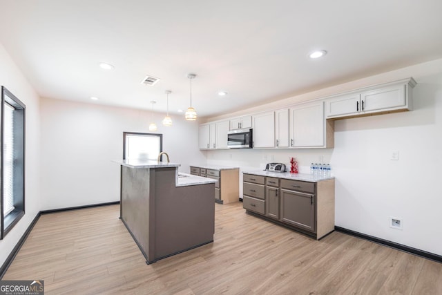 kitchen featuring a healthy amount of sunlight, a center island with sink, light hardwood / wood-style floors, and decorative light fixtures