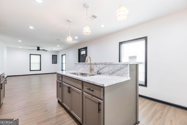 kitchen featuring sink, a center island with sink, light hardwood / wood-style floors, and decorative light fixtures