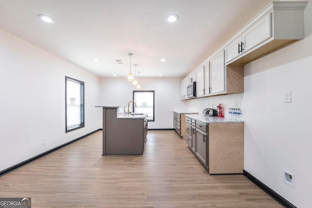 kitchen featuring light stone counters, hanging light fixtures, light hardwood / wood-style flooring, sink, and a center island with sink