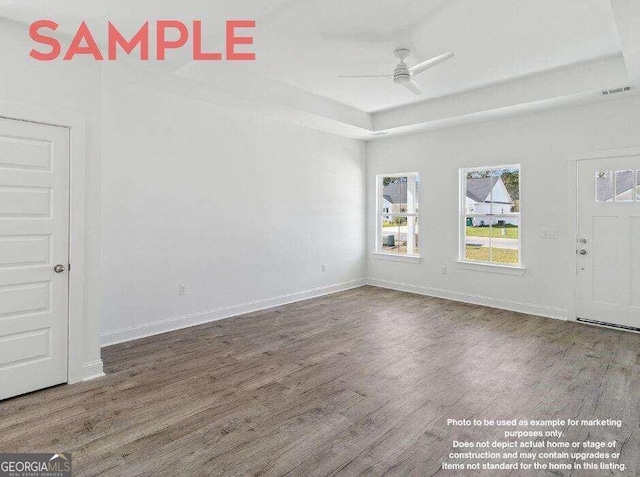 empty room featuring ceiling fan, dark hardwood / wood-style flooring, and a tray ceiling