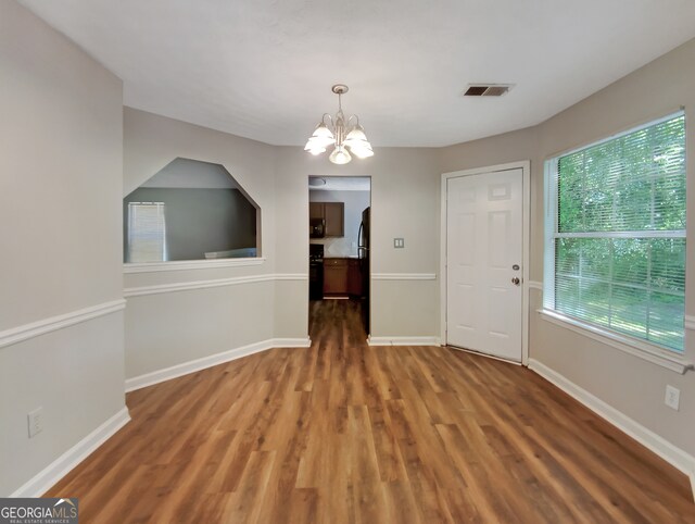 empty room featuring a notable chandelier, plenty of natural light, and hardwood / wood-style flooring