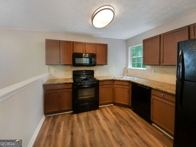 kitchen featuring sink, light stone countertops, hardwood / wood-style flooring, and black appliances