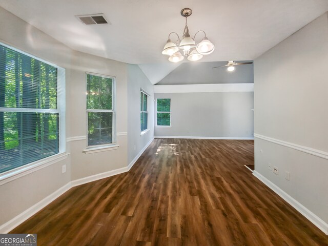 empty room with ceiling fan with notable chandelier, plenty of natural light, dark wood-type flooring, and vaulted ceiling