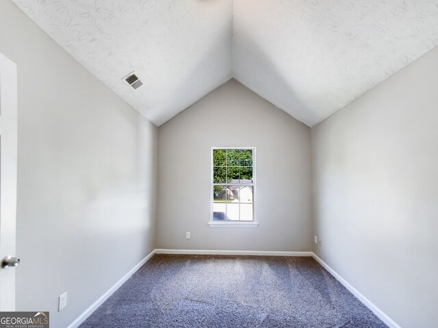 spare room featuring a textured ceiling, vaulted ceiling, and carpet flooring