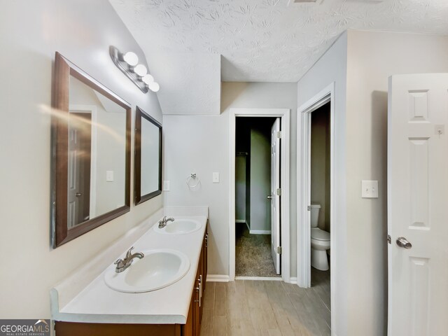 bathroom with large vanity, double sink, hardwood / wood-style flooring, toilet, and a textured ceiling