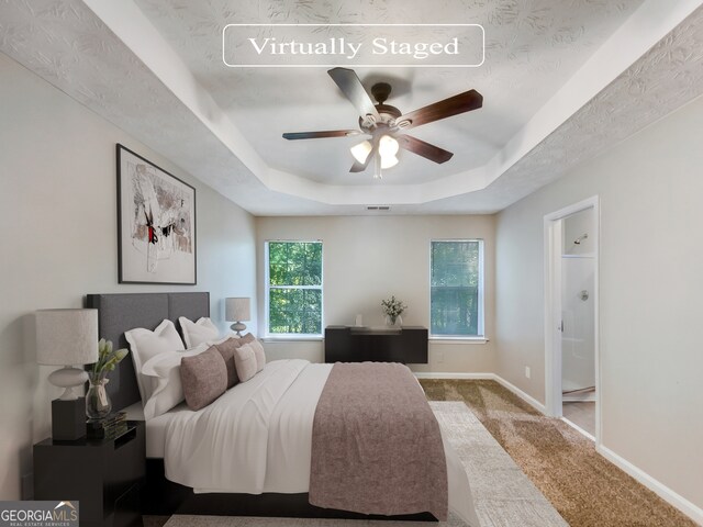 carpeted bedroom featuring connected bathroom, ceiling fan, and a tray ceiling