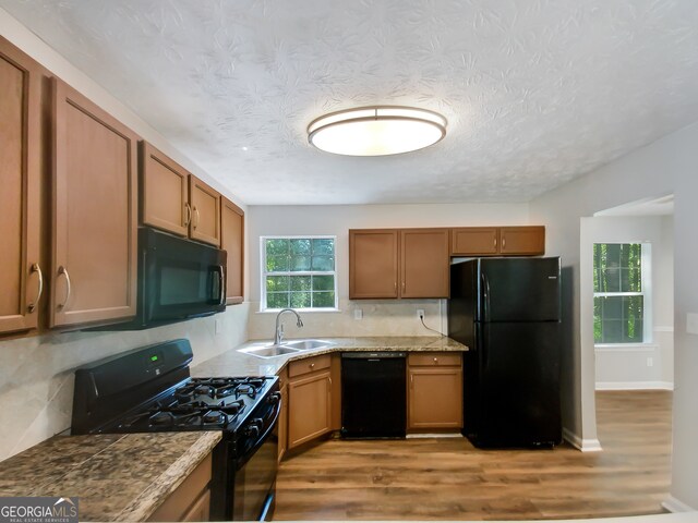 kitchen featuring a textured ceiling, black appliances, sink, and light wood-type flooring