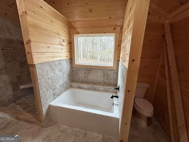 bathroom featuring a washtub, wood walls, toilet, and tile floors