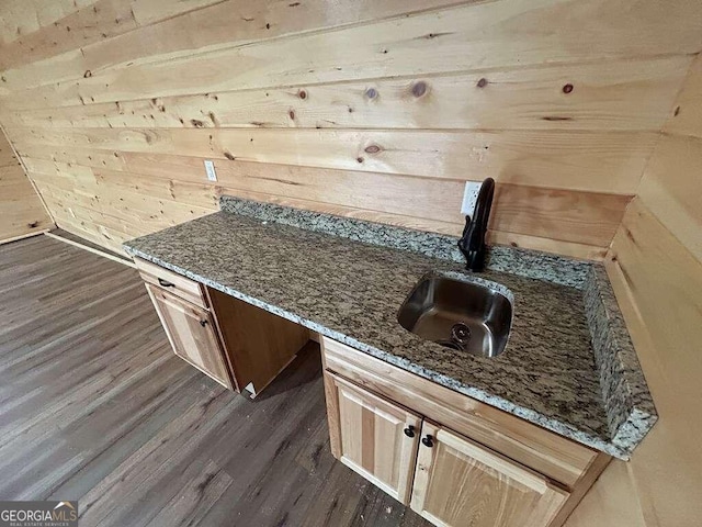 kitchen with wood walls, dark wood-type flooring, dark stone counters, and sink