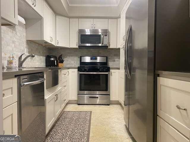 kitchen with backsplash, stainless steel appliances, white cabinets, light tile floors, and ornamental molding