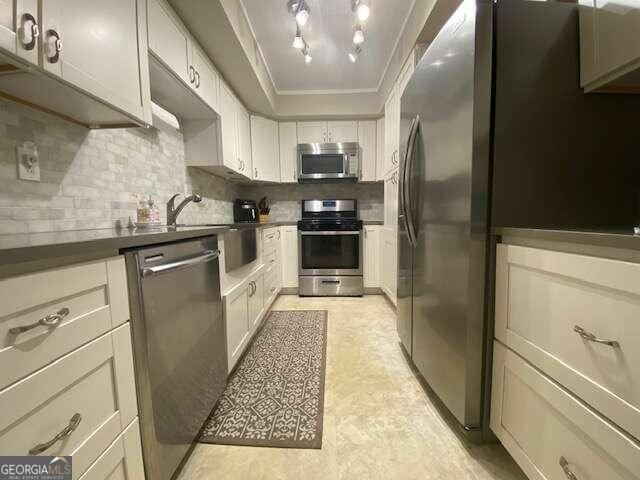 kitchen with stainless steel appliances, crown molding, light tile flooring, track lighting, and tasteful backsplash