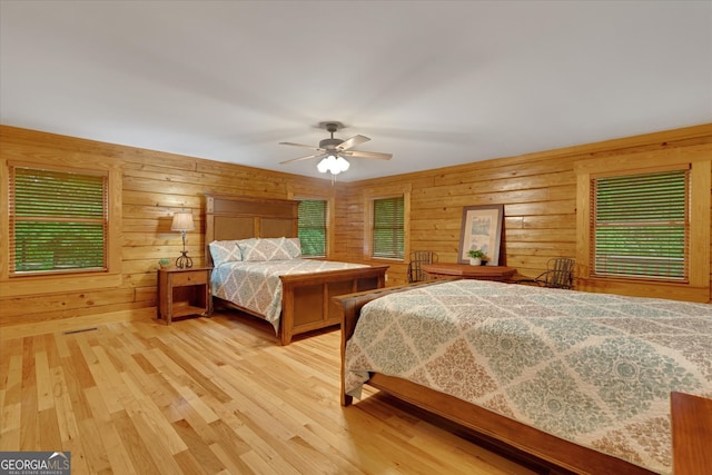 bedroom with light hardwood / wood-style floors, ceiling fan, and wood walls